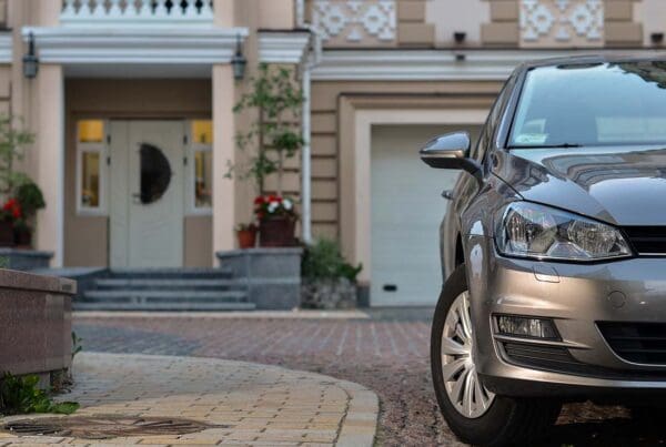 Home and Auto Insurance (Bundled) - Close-up View of a Luxury Car Parked in Front of a Large Modern Home Blurred in the Distance