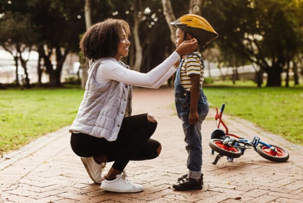 Group Voluntary Supplemental Life Insurance - Mother Placing a Protective Helmet on Her Son Before Riding a Bike in the Park on a Sunny Day